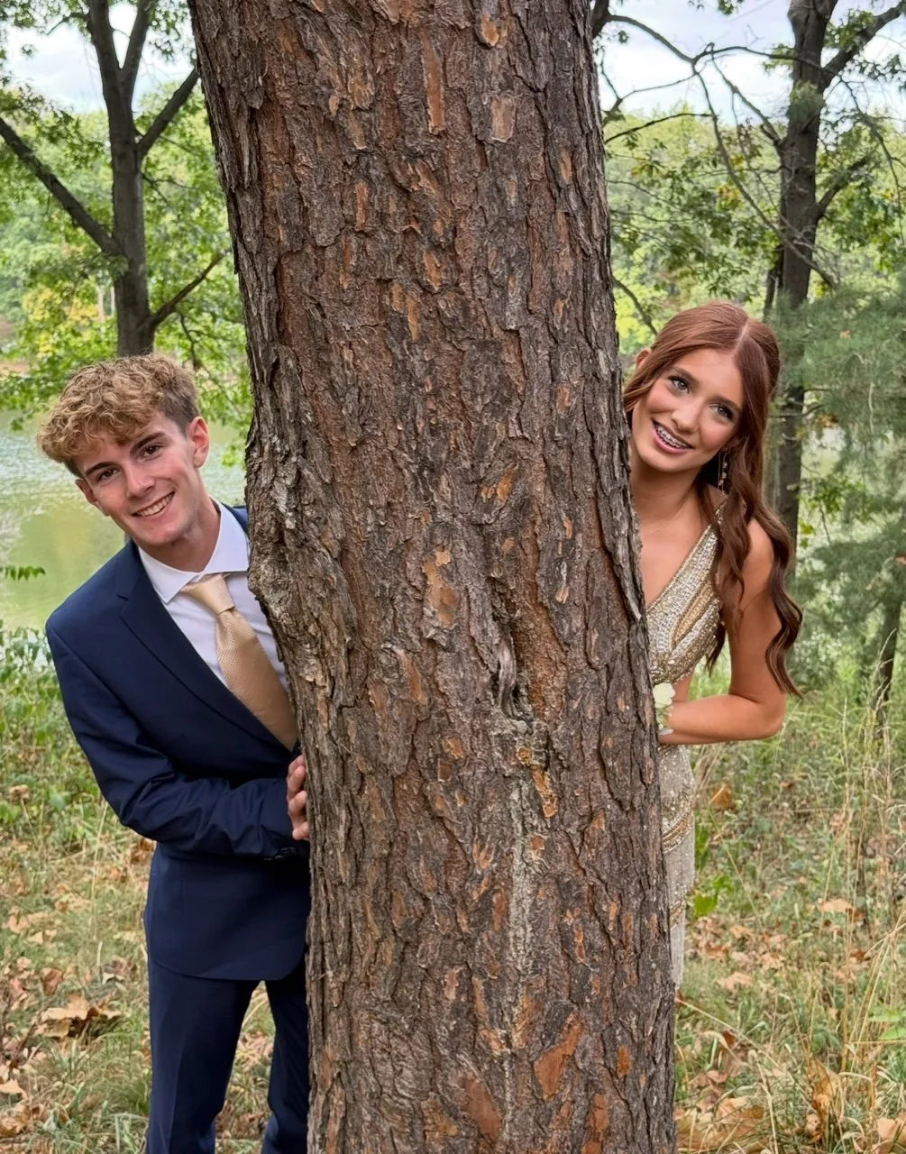 Two people in formal clothing beside a tree